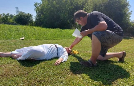 Kobieta leży na trawniku pochyla  się nad nią mężczyzna 