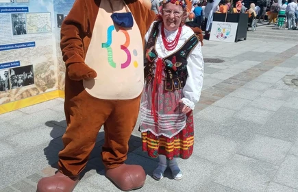 Zdjęcie pozowane osoba w stroju regionalnym Krakowskim w objęciach wielkiego misia