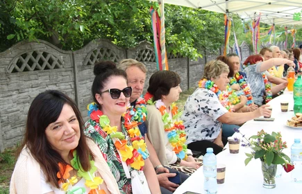 kobiety siedzące przy nakrytym stole, na szyjach mają kwiatowe wianki